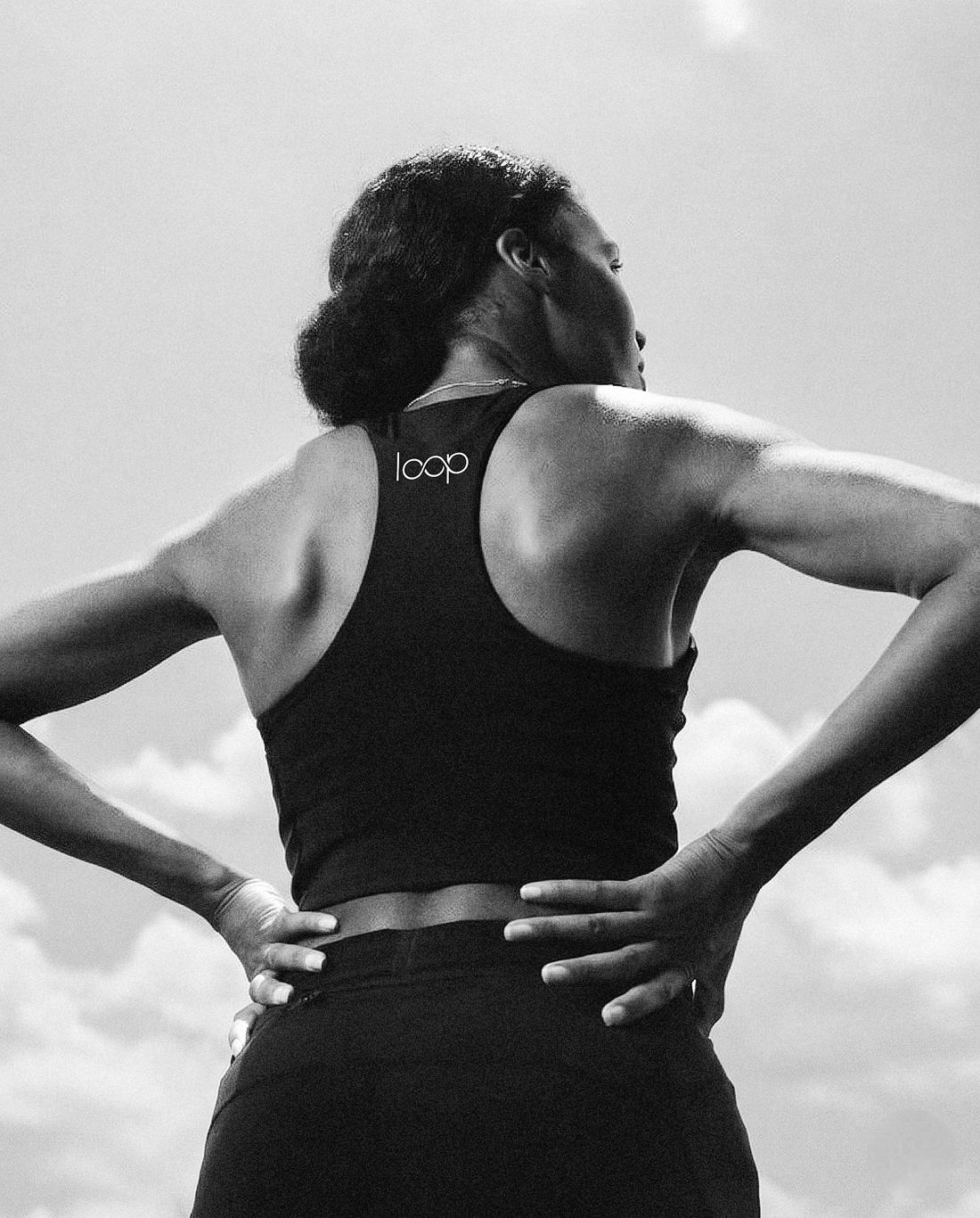 Athlete with hands on hips, seen from behind, wearing a black Loop racerback top